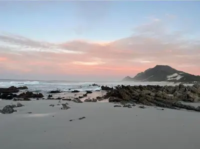 a beach with a mountain in the background and the ocean at Brandys beach house bettys bay in Bettyʼs Bay