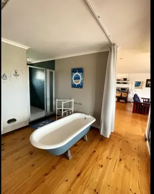 a large bath tub in a room with a wooden floor at Brandys beach house bettys bay in Bettyʼs Bay