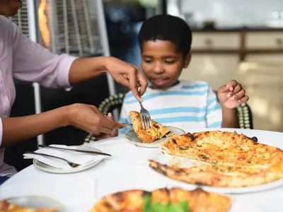 a young boy sitting at a table eating pizza at Century City Hotel Bridgewater in Cape Town