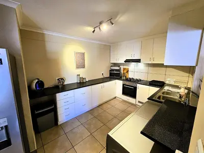a kitchen with white cabinets and black counter tops at Walters Lane Deluxe Garden Apartment 3 - No loadshedding in Cape Town