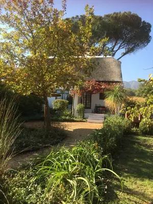 a cottage with a thatched roof in a garden at Mooi Bly in Paarl
