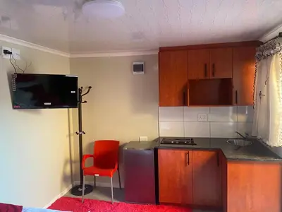 a kitchen with a red chair and a counter and a television at SABATH LODGE in Cape Town