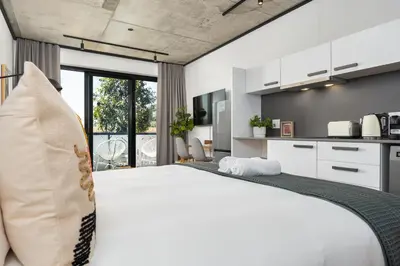 a bedroom with a white bed and a kitchen at Bridgewater One Apartments in Cape Town