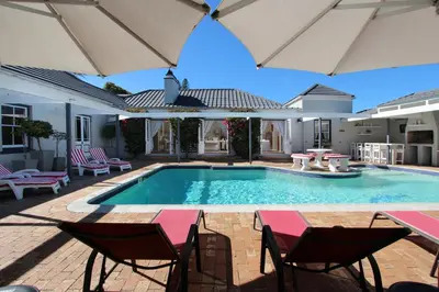 a swimming pool with chairs and umbrellas at 19th Hole Guest Lodge - Golfers paradise in Hermanus
