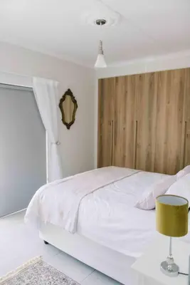 a bedroom with a white bed with a wooden headboard at Bright and airy Parisian Gem close to the beach in Cape Town