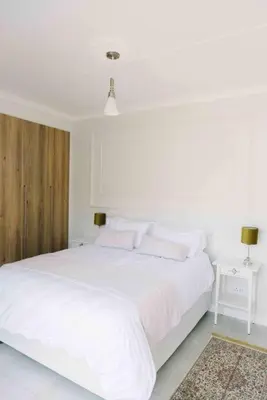 a white bedroom with a large bed with white sheets and pillows at Bright and airy Parisian Gem close to the beach in Cape Town