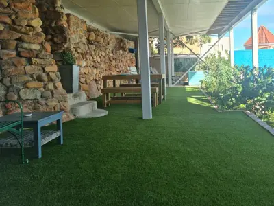 a patio with a stone wall and green grass at The Anchor, Luxury living for 2 with sea view and Jacuzzi in Gordonʼs Bay
