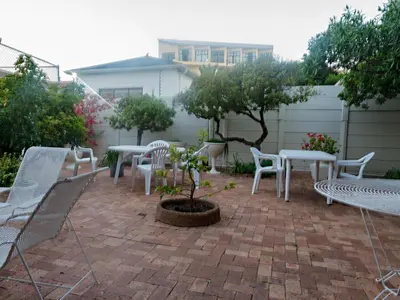 a patio with white chairs and tables and trees at Ocean-Song in Strand
