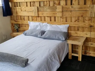 a bedroom with a wooden wall with a bed at Sunset beach backpackers in Bloubergstrand
