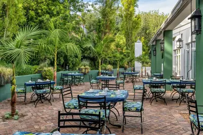 a patio with tables and chairs and palm trees at Lord Charles Hotel, Somerset West, a Tribute Portfolio Hotel in Somerset West