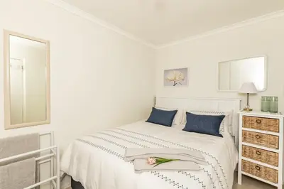 a white bedroom with a white bed with blue pillows at Suburban bliss with Wifi and plunge pool in Cape Town