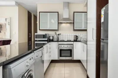 a kitchen with white cabinets and a washer and dryer at The Manhattan Apartments in Cape Town