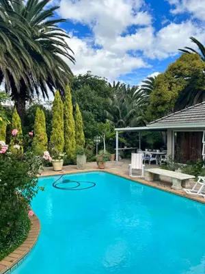a large blue swimming pool with a patio and trees at Somerset West All Stay 1 in Somerset West