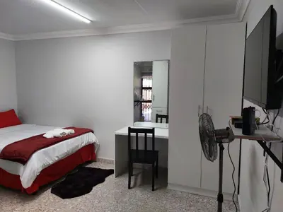 a bedroom with a bed and a desk and a kitchen at Finca Guest House in Cape Town
