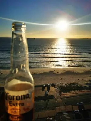 a bottle of corona beer sitting on the beach with the sunset at Horizon Bay 1502 in Cape Town
