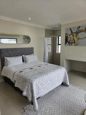 a bedroom with a large bed with a white blanket at LND GUEST HOUSE in Bloubergstrand