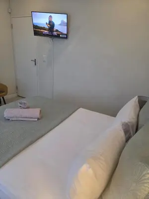 a bedroom with a white bed with a tv on the wall at LND GUEST HOUSE in Bloubergstrand