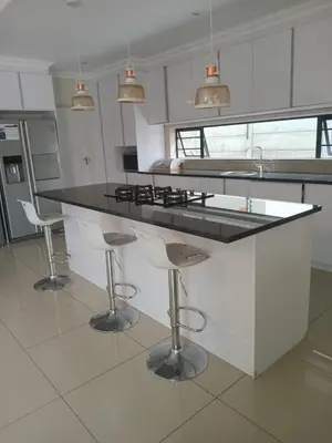 a kitchen with a black counter and stools at LND GUEST HOUSE in Bloubergstrand