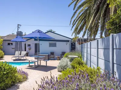 a backyard with a pool and a house with umbrellas at Southeaster in Bloubergstrand