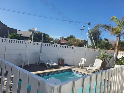 a swimming pool with chairs and a white fence at The White House Lodge in Cape Town