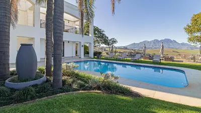 a swimming pool in front of a house with a palm tree at The Salene Hotel & Apartments in Stellenbosch