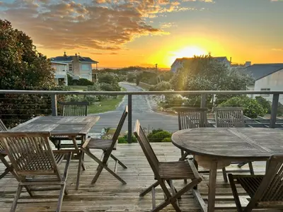 a wooden table and chairs on a deck with the sunset at 82 Steps to the Beach in Pringle Bay