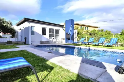 a swimming pool with blue chairs and a house at 82 Steps to the Beach in Pringle Bay