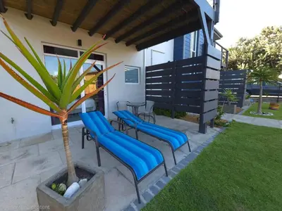 a patio with blue chairs and a palm tree at 82 Steps to the Beach in Pringle Bay