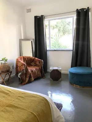 a bedroom with a bed and a chair and a window at Bird Song Cottage - Table View in Cape Town