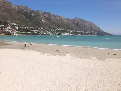 a sandy beach with a town and mountains in the background at Helderberg Guesthouse in Gordonʼs Bay