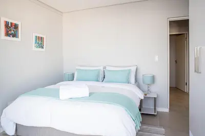 a white bedroom with a large bed with blue pillows at Beachfront 2 bed w swimming pool, Blouberg 54 Beach Break in Bloubergstrand