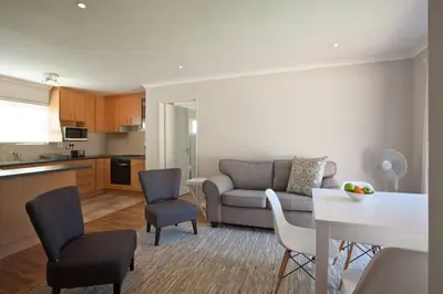 a living room with a couch and chairs and a kitchen at Sunbird Cottage in Somerset West