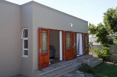 a white house with wooden doors and a porch at Sunbird Cottage in Somerset West