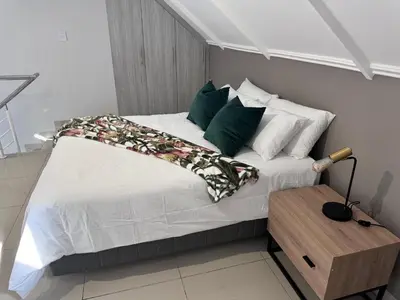 a bed with green and white pillows and a table at Beautifully furnished loft apartment in central Durbanville in Durbanville