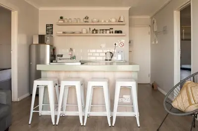 a kitchen with three white stools at a counter at Easy Going Hermanus With An Ocean View in Hermanus