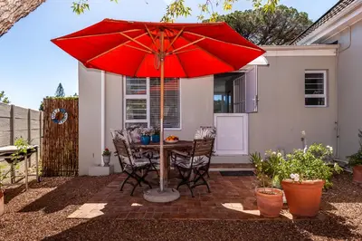 a table and chairs under a red umbrella on a patio at Tortelduif Cottage in Stellenbosch