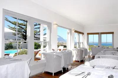 a restaurant with white tables and white chairs and windows at 11 WESTCLIFF RENTALS in Hermanus