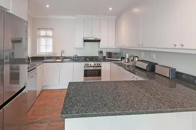 a large kitchen with white cabinets and granite counter tops at Mountain View by Top Destinations Rentals in Hermanus