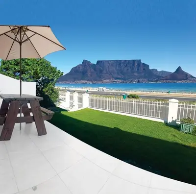 a picnic table with an umbrella and a view of the beach at Cap du Mont in Bloubergstrand