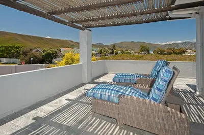a patio with wicker chairs and pillows on a balcony at Villa Venusta Luxury Guesthouse - Solar Power in Hermanus