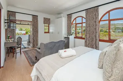 a bedroom with a white bed and a chair and windows at Villa Venusta Luxury Guesthouse - Solar Power in Hermanus