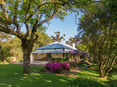a house with a blue roof in a park with purple flowers at Bartholomeus Klip Farmhouse at Elandsberg Nature Reserve in Hermon