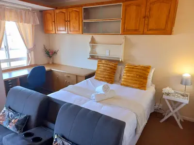 a bedroom with a bed and two blue chairs at Cozy Strand Beach Getaway - Studio Apartment in Cape Town