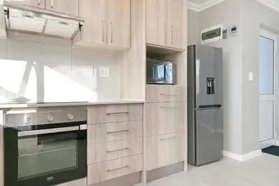 a kitchen with wooden cabinets and a stainless steel refrigerator at Stunning, Luxurious Apartment close to the beach in Cape Town