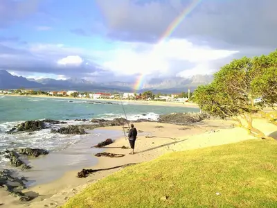 a person fishing on the beach with a rainbow in the sky at Milkwood Cottage, Beachfront family vacation home, Sleeps 6 in Gordonʼs Bay