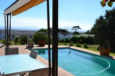 a swimming pool with a table next to a house at Saxenburg Wine Farm in Kuilsrivier