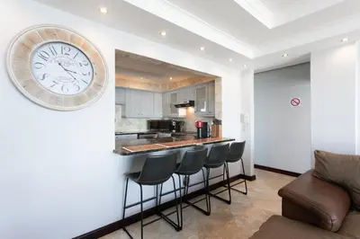 a kitchen with a bar with stools and a clock on the wall at Luxury Witsand 706 in Cape Town