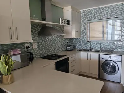 a kitchen with white cabinets and a washer and dryer at Lagoon Beach Apartment 309 in Cape Town