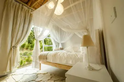 a bedroom with a bed with white curtains and a window at Stonehaven Eco Cabins in Hermanus