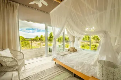 a bedroom with a canopy bed and a large window at Stonehaven Eco Cabins in Hermanus
